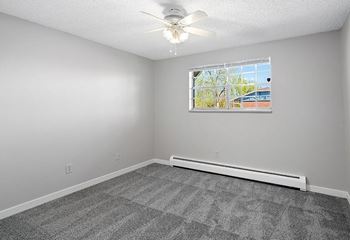 A room with a ceiling fan and a window with a view of a building outside.